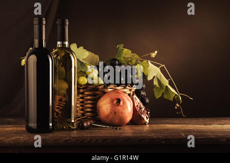 Wine bottles, corkscrew and grapes in a basket on a wooden table, wine tasting still life Stock Photo