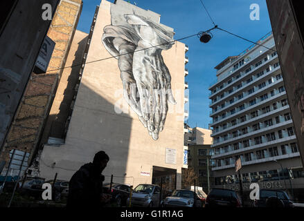 A street art mural in the form of a giant pair of praying hands looms over Pireos street in the Omonia district of Athens,Greece Stock Photo