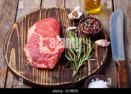 Raw fresh meat Steak with salt and pepper, rosemary and tomatoes on cutting board on dark wooden background. Copy space Stock Photo
