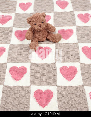 teddy bear sat on rug with hearts and squares Stock Photo