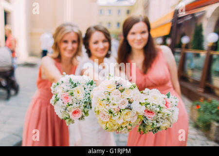 Two bridesmaids in peach dress and bride on background with luxury bouquets Stock Photo