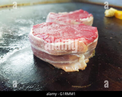 Raw beef, fillet mignon tournedous, wrapped with bacon, getting fried on a frying table, at a restaurant kitchen Stock Photo