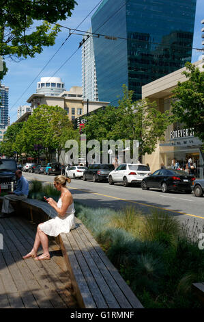 Woman sitting on a bench using her smart phone on Robson Street in downtown Vancouver, BC, Canada Stock Photo
