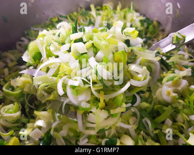 Metal spoon full of fried leek, inside a metal pot Stock Photo