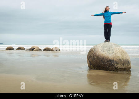 Young woman posing on top of one Moeraki Boulder on the Koekohe beach, Eastern coast of New Zealand Stock Photo