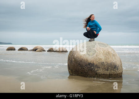 Young woman posing on top of one Moeraki Boulder on the Koekohe beach, Eastern coast of New Zealand Stock Photo