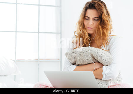 Pensive woman in pajamas using laptop computer on the bed at home Stock Photo
