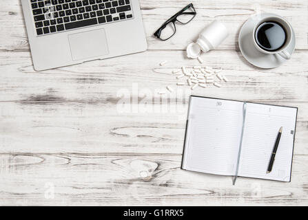 Office workplace with cup of coffee, laptop and medicine capsules. Health, stress and tiredness concept Stock Photo