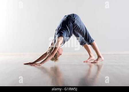 Single young short haired blond woman performing downward facing dog yoga pose on hardwood floor Stock Photo