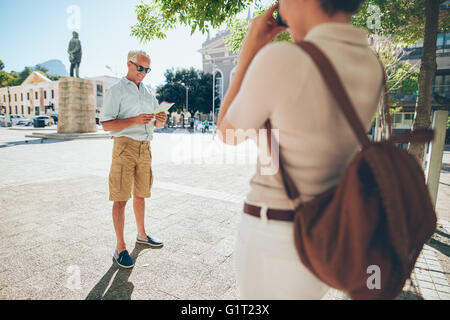 Senior man being photographer by a woman in the city during their vacation. Senior couple taking photos on their vacation. Stock Photo