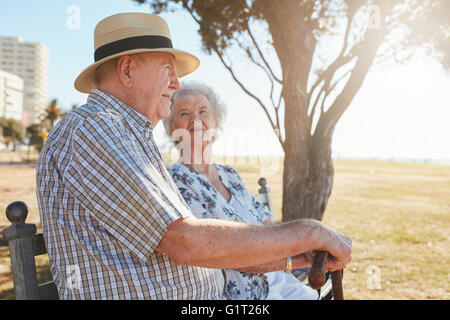 Side view shot of elderly man and woman sitting on a bench outdoors. Senior couple sitting on a park bench. Stock Photo