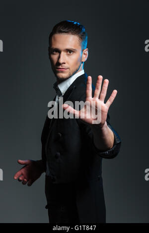 Handsome young man magician showing his palm over grey background Stock Photo