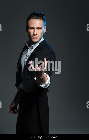 Attractive mysterious young magician holding something on palm over grey background Stock Photo