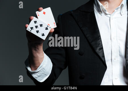 Closeup of man magician with two playing cards in his hand over grey background Stock Photo