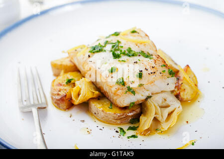 Roasted cod, codfish with baked potatoes and artichokes with lemon and herbs sauce Stock Photo
