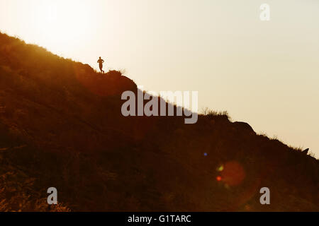 Silhouette of runner ascending hillside at sunset Stock Photo