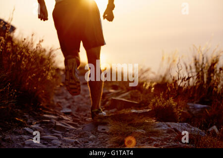 Man running on craggy trail at sunset Stock Photo