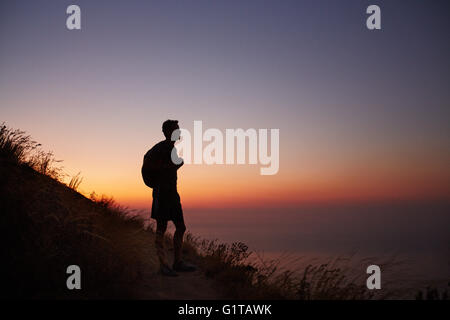 Silhouette of male hiker on trail overlooking ocean at sunset Stock Photo