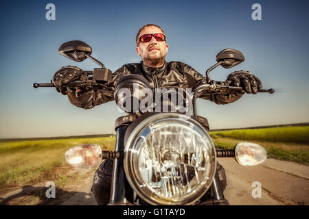 Biker in a leather jacket riding a motorcycle on the road. Filter applied in post-production. Stock Photo