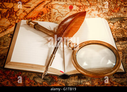 Vintage still life - magnifying glass, old book and goose quill pen lying on an old map in 1565. Stock Photo