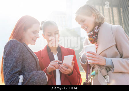 Women texting and drinking coffee outdoors Stock Photo