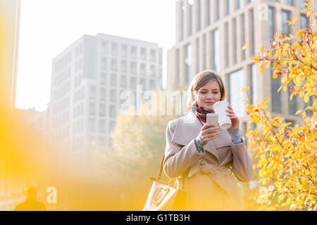 Businesswoman texting and drinking coffee in city Stock Photo