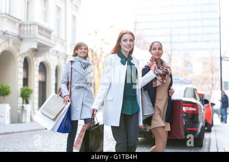 Smiling women with shopping bags crossing city street Stock Photo