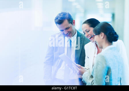 Business people with digital tablet laughing in office corridor Stock Photo