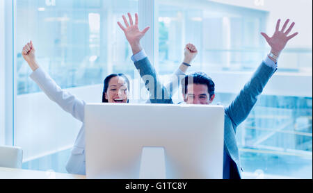 Exuberant businessman and businesswoman cheering with arms raised at computer in office Stock Photo