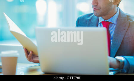 Focused businessman reviewing paperwork at laptop in office Stock Photo