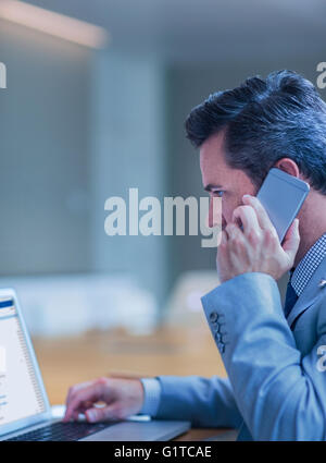 Businessman talking on cell phone and working at laptop in conference room Stock Photo