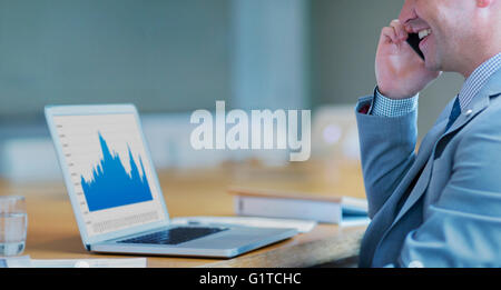 Smiling businessman talking on cell phone at laptop in conference room Stock Photo