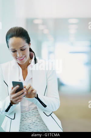 Smiling businesswoman using cell phone in office corridor Stock Photo