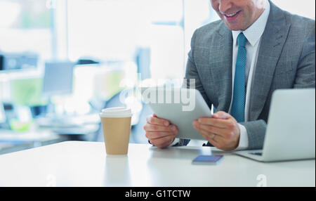 Smiling businessman using digital tablet with coffee in office Stock Photo