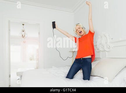 Playful women kneeling on bed listening to music with mp3 player and headphones Stock Photo