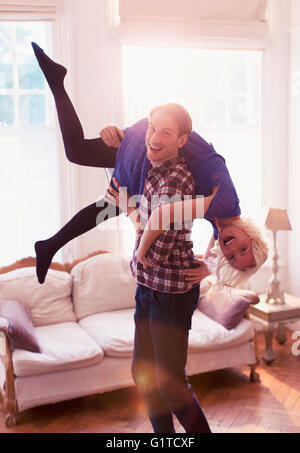 Portrait playful husband carrying wife over shoulder in living room Stock Photo