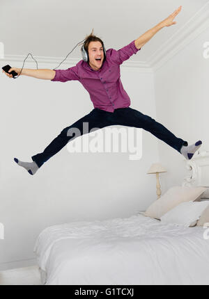 Playful man jumping on bed with legs apart listening to music with mp3 player and headphones