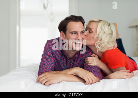 Affectionate wife kissing smiling husband on bed Stock Photo