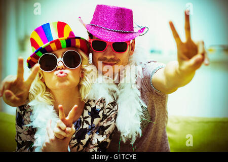 Portrait playful couple in costume sunglasses and hats gesturing peace sign Stock Photo