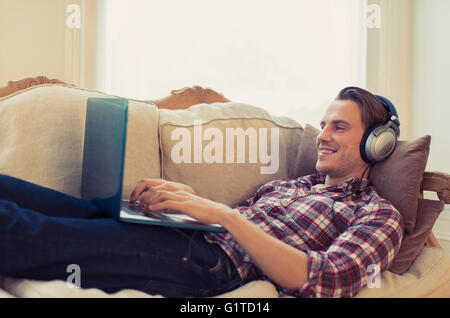 Man with headphones using laptop on living room sofa Stock Photo
