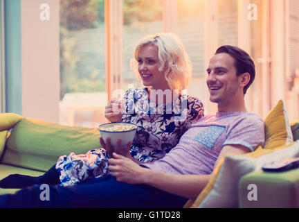 Couple watching TV and eating popcorn on living room sofa Stock Photo