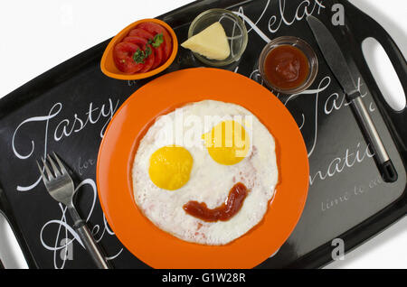 Boiled eggs with omelets displayed on orange plate with tomato sauce, cheese cube and sliced tomatoes, Black tray on white backg Stock Photo