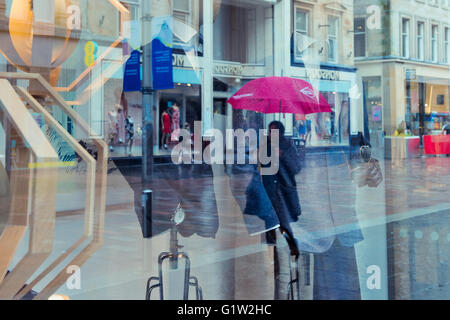 Shoppers are reflected in shop windows in Buchanan Street, Glasgow in the rain. Stock Photo