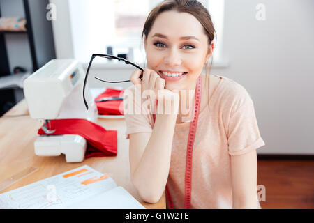 Cheerful attractive young woman seamstress sitting and smiling at work Stock Photo