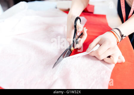 Hands of young woman seamstress with scissors cutting white fabric Stock Photo