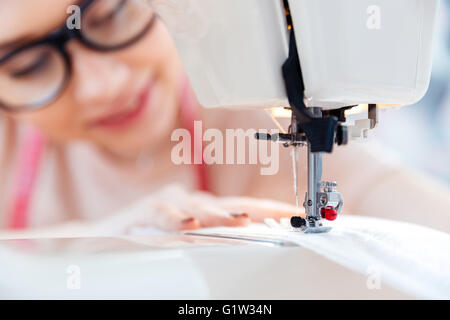 Happy young woman in glasses sews on the sewing machine Stock Photo