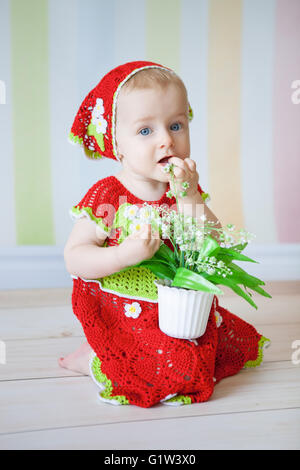 Little girl sitting on floor dressed in red reding hood  costume and holding pot with flowers in her hands Stock Photo
