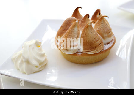 Lemon tart with meringue and whipped cream on white square plate Stock Photo