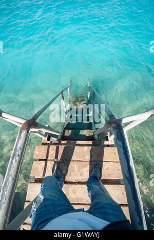 Old vintage metal wooden stairs leading to blue turquoise sea water from beach. Beautiful summer day. Swimming pool with grunge retro stairs on the ocean coast. Top POV, Point of view shot Stock Photo