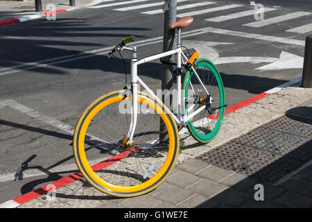 A colored bicycle locked to a post on the pavement Stock Photo